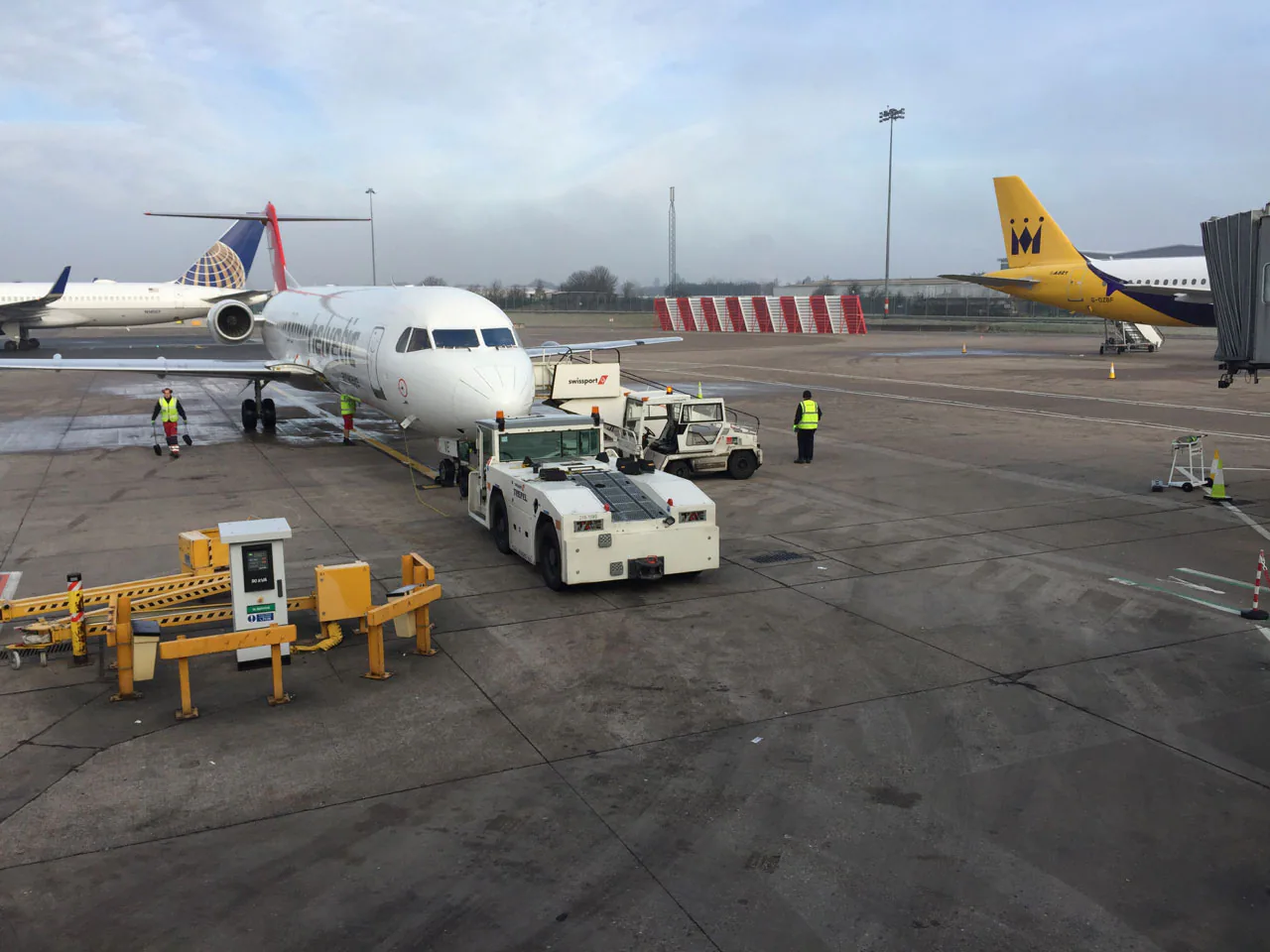 Aircraft, ground crew and towing vehicles operating on an airport apron.