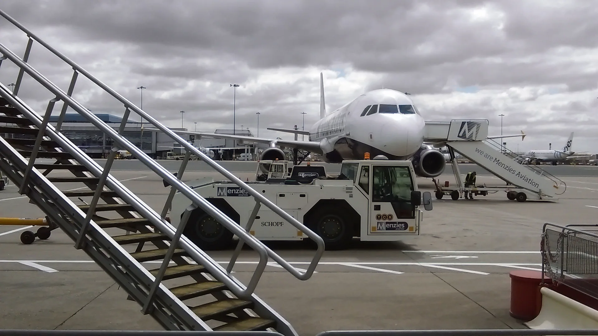 Aircraft with a pushback tug and passenger steps on an airport apron.