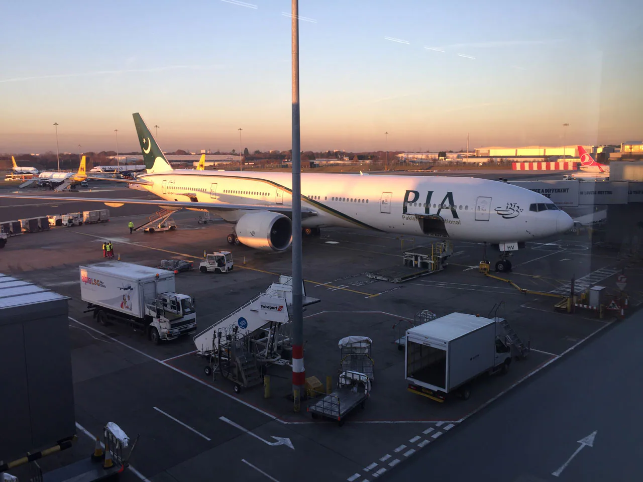 Passenger aircraft, ground crew and service vehicles on an airport stand at sunset.