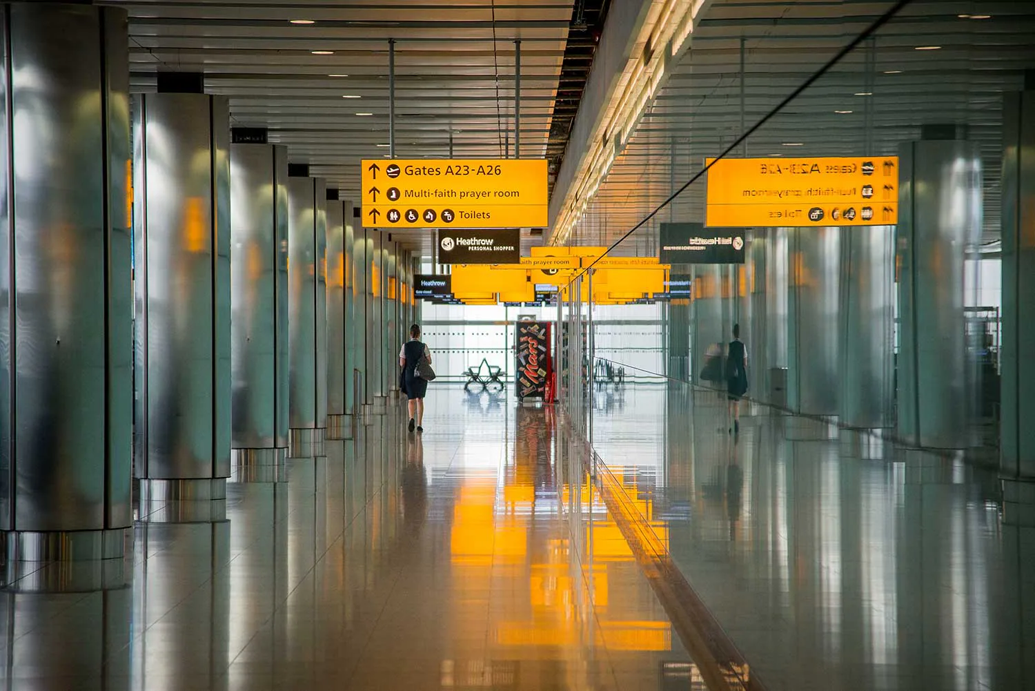 Airport terminal corridor with yellow wayfinding signs and reflective glass.