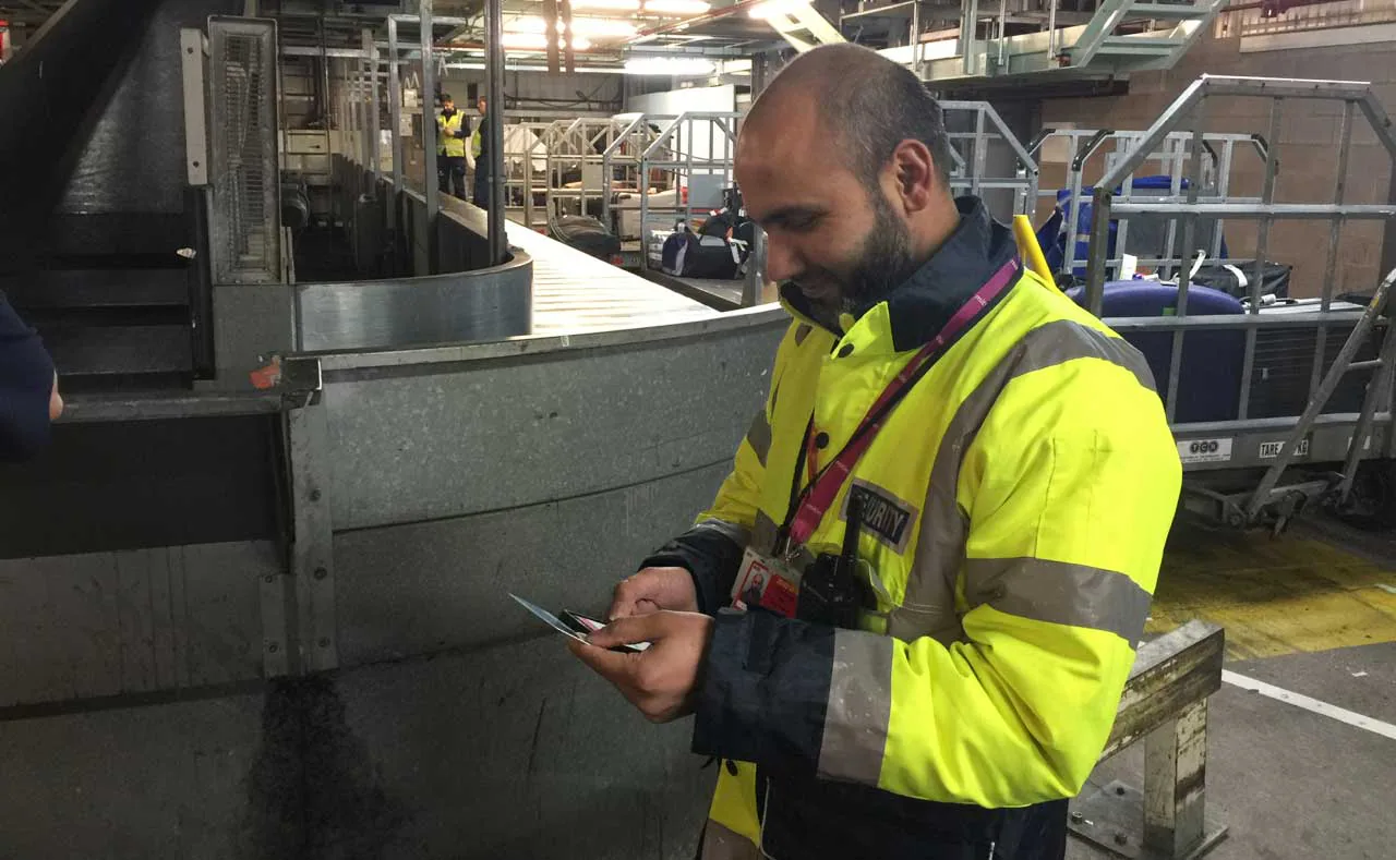 Security officer using a mobile device beside baggage handling equipment.